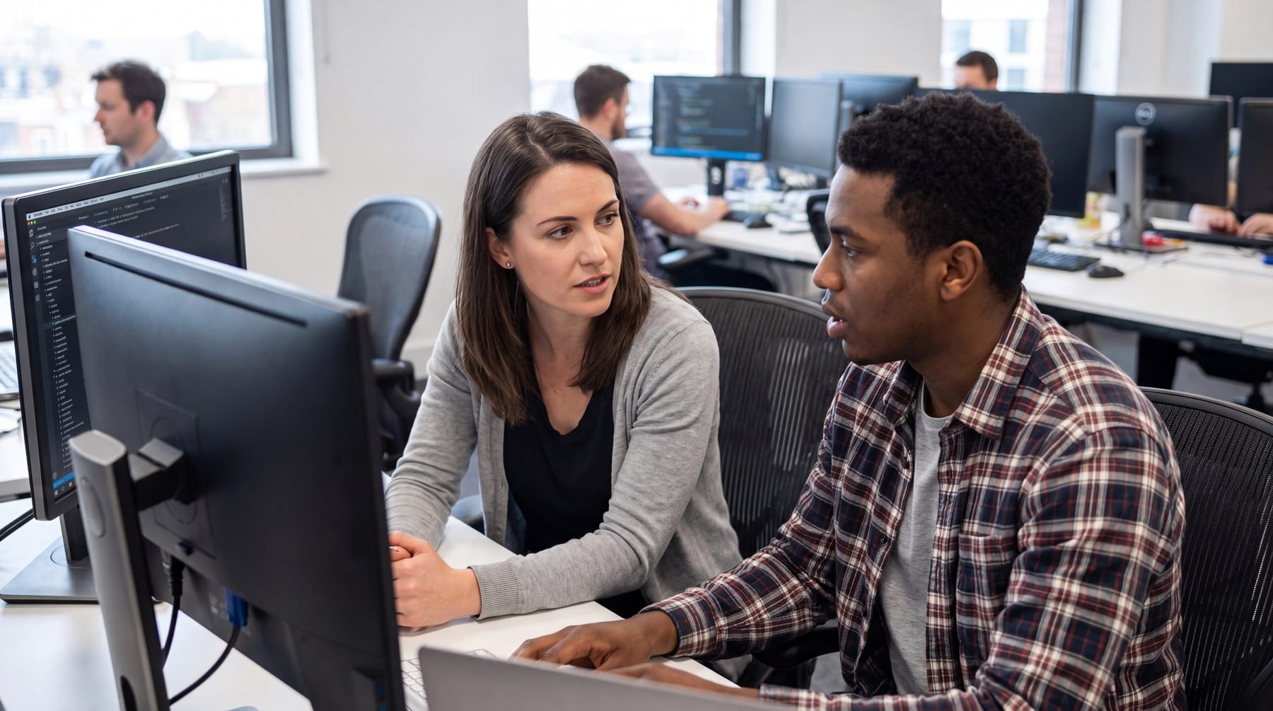 Two colleagues talking through a problem at one monitor in an open office.