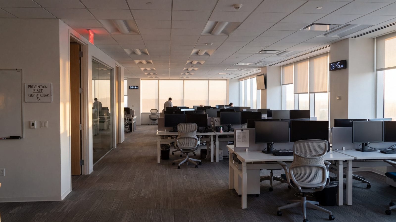 An empty open-plan office at 06:45, chairs neat, screens off, morning light.
